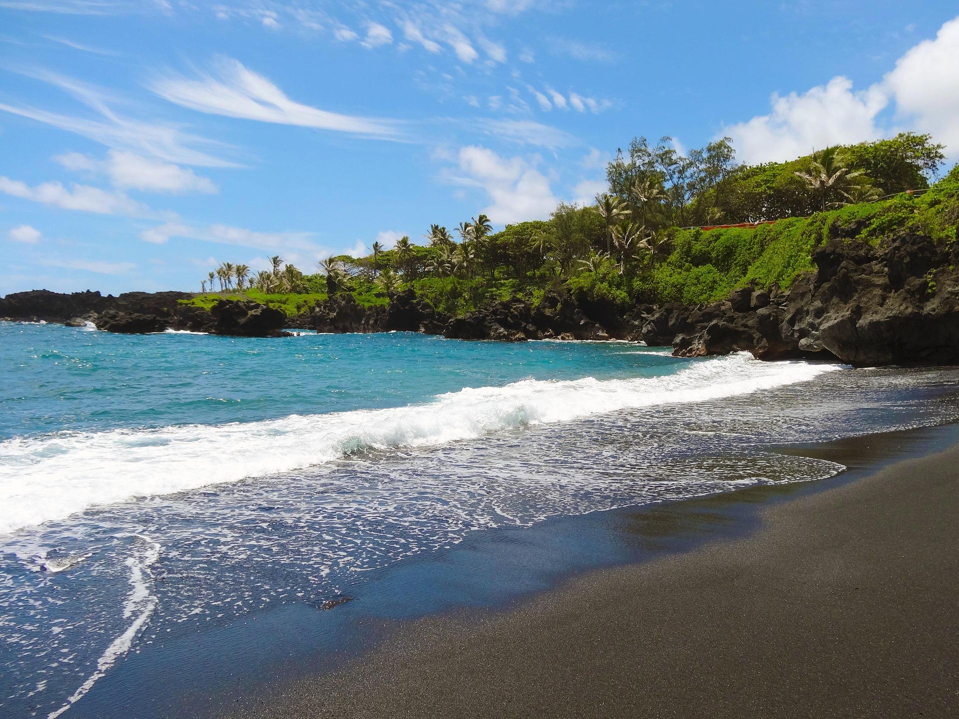 Black sand beach with turquoise waves and green, palm-covered lava cliffs in Maui, Hawaii